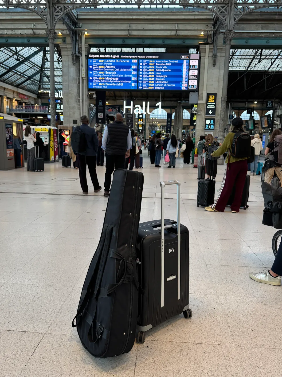 Guitar case and suitcase beneath the departure board in a railway station