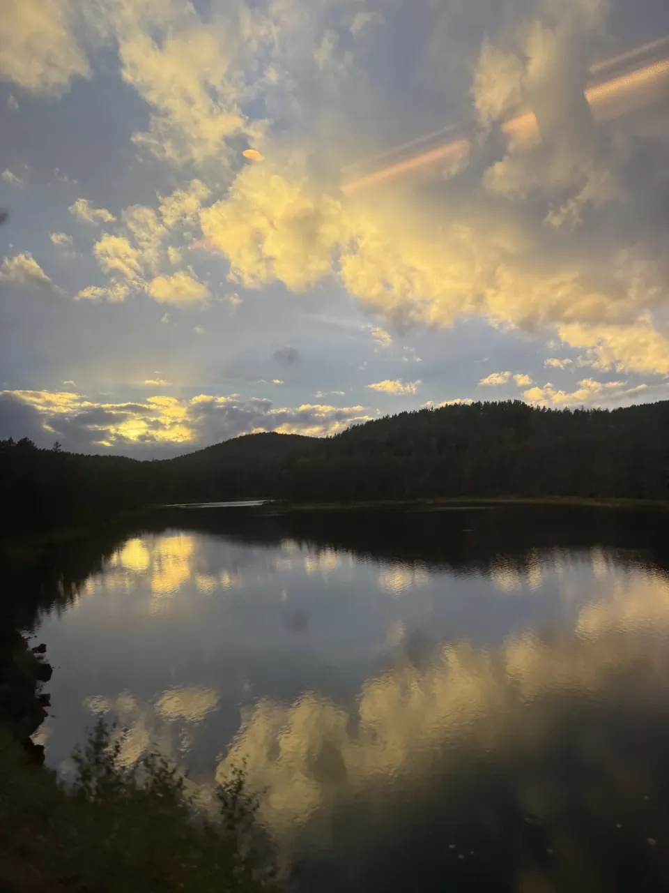 Golden clouds and Norwegian hills reflected in a lake, seen from the train